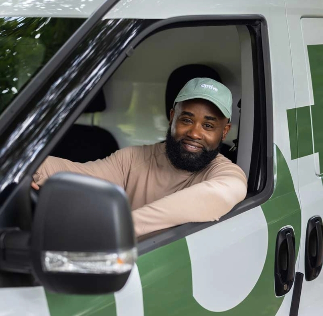An Aptive Pest Control Specialist Smiling While Seated In The Driver'S Seat Of A Company Vehicle